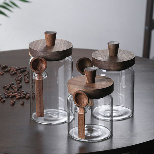 Three glass jars with wooden lids and handles on a table with coffee beans.